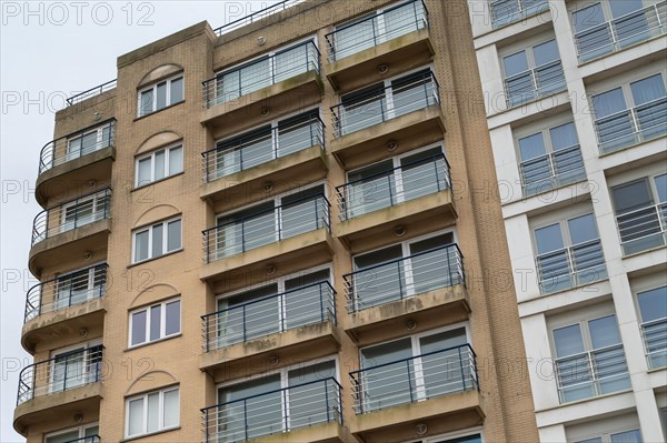 Multi-storey residential building with balconies and architectural decorations under a cloudy sky,