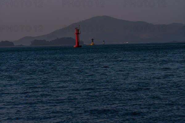 Three small light houses in a harbor with small mountains shrouded in fog and mist in the