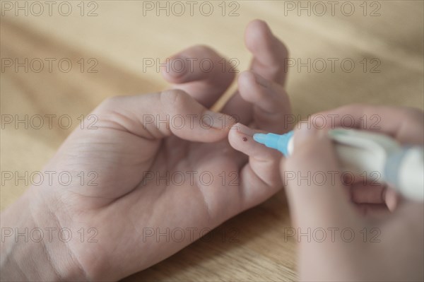 On the left a child's hand with a drop of blood on the little finger, in the right hand the child