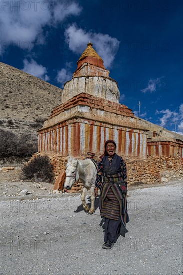 Woman with her horse, colourfully painted Buddhist stupa in front of mountain landscape, erosion