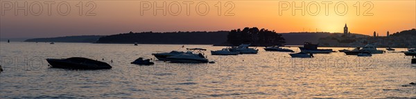 Boats anchoring in a bay, silhouette of a church tower, sunset over Rab, panoramic view, town of