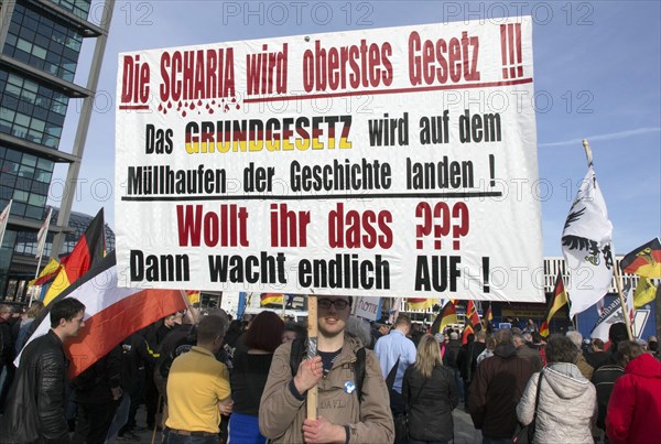 A participant in the Merkel muss weg demonstration holds a poster with the inscription Die Scharia
