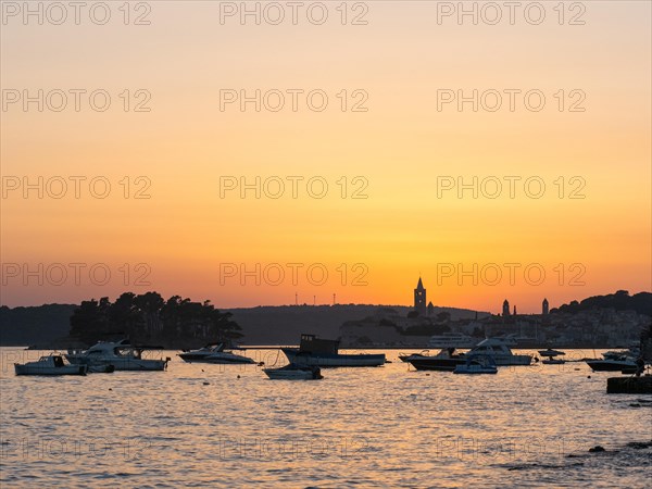 Boats anchoring in a bay, silhouette of church towers, evening mood after sunset over Rab, town of