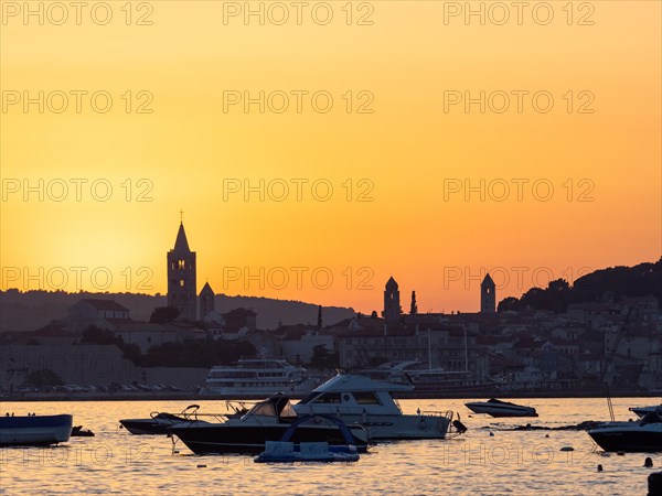 Boats anchoring in a bay, silhouette of church towers, evening mood after sunset over Rab, town of