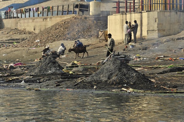 Busy riverbank full of people and animals, smoke and pollution emphasise the daily drama, Varanasi,