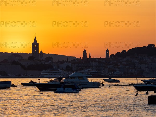 Boats anchoring in a bay, silhouette of church towers, evening mood after sunset over Rab, town of
