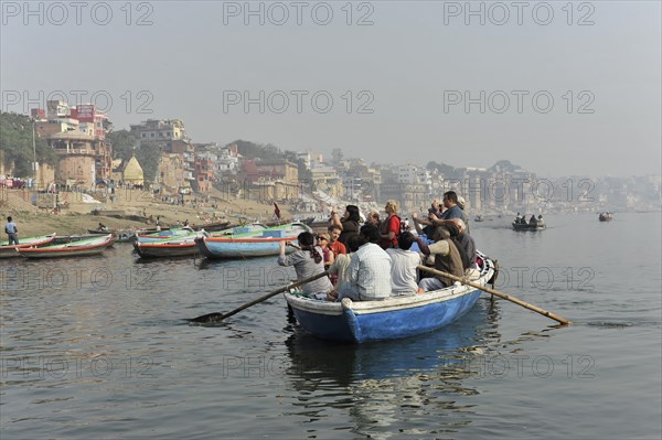 Boat with passengers on a river, rowers at the stern, city view in the light morning mist in the