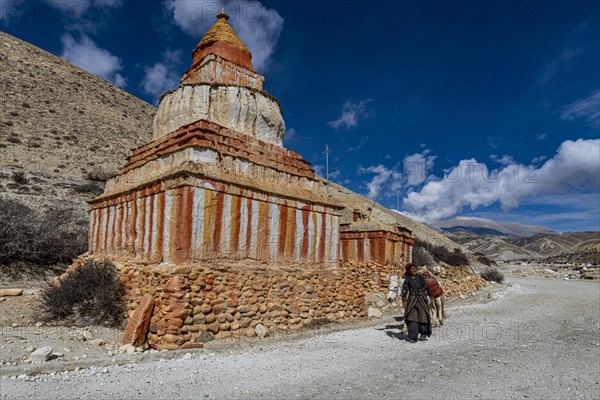 Woman with her horse, colourfully painted Buddhist stupa in front of mountain landscape, erosion