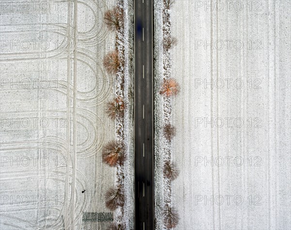 An aerial view shows an avenue with trees leading through snow-covered fields on which tyre tracks