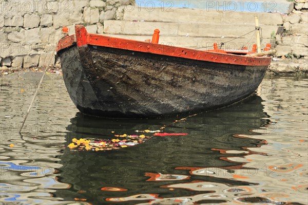 A single boat floats with a flower offering on the calm waters of a river in India, Varanasi, Uttar