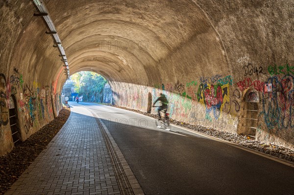 A person on a bicycle rides through a tunnel decorated with graffiti, Nordbahntrasse, Elberfeld,