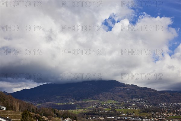 Mighty white spring clouds move under a blue sky over a wooded hill near Jongny, Jongny,