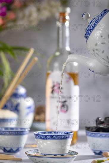Pouring tea, Asian tea set with blue patterns, a bottle of China plum wine in the background, dried