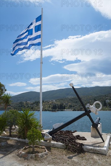 Greek flag flying next to a large anchor and cannon overlooking the sea and coastal landscape,