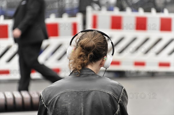 A person with headphones stands in front of a roadblock, taken from behind, Hamburg, Hanseatic City