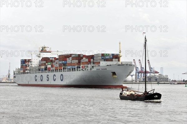 A large container ship next to a small sailing boat in a cloudy harbour, Hamburg, Hanseatic City of