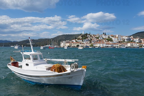 A fishing boat on the sea in front of a picturesque coastal town under a partly cloudy blue sky,