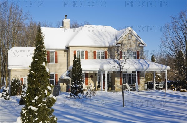 Two story beige vinyl siding with brownish red nuanced brick veneer and orange trim home in winter,