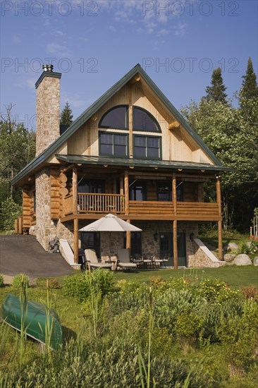 Handcrafted two story spruce log home cabin with fieldstone chimney, green sheet metal roof and