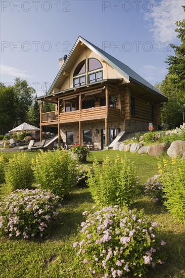 Handcrafted two story spruce log cabin home with fieldstone chimney and green sheet metal roof in