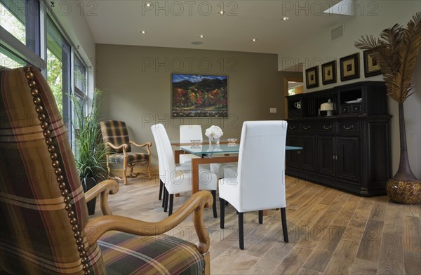Clear glass top table and white leather high back chairs in dining room with beige ceramic tile