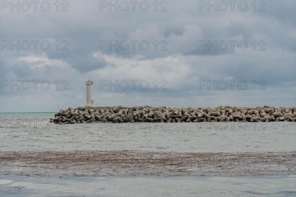 White lighthouse on a protective stone breakwater jutting out into a cloudy sea, in Ulsan, South