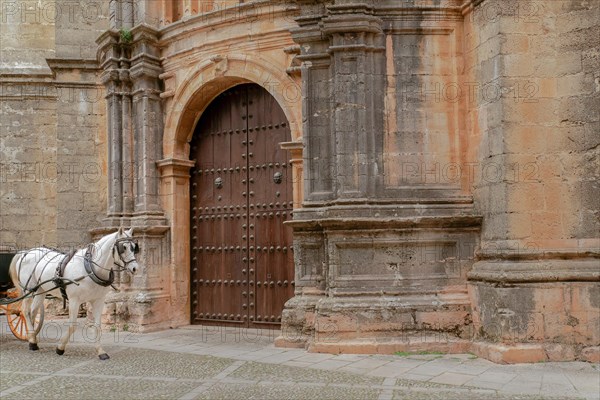 A horse-drawn carriage with a white horse drives past the door of a church with an imposing stone