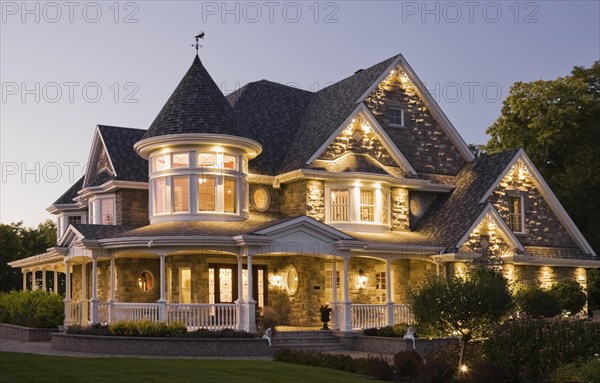 Elegant grey stone with white trim and blue asphalt shingles roof Victorian home facade at dusk in