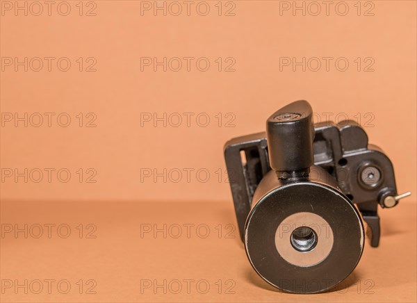 Closeup bottom view of quick release tripod head on brown background. Selective focus on thread for