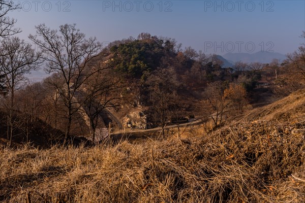 Section of mountain fortress wall behind leafless trees on top on winter morning with clear blue