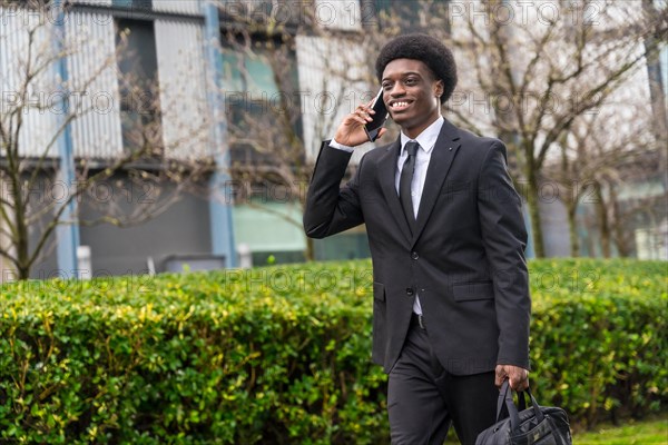 Three quarter length portrait of a cool smiling african businessman walking along the street using
