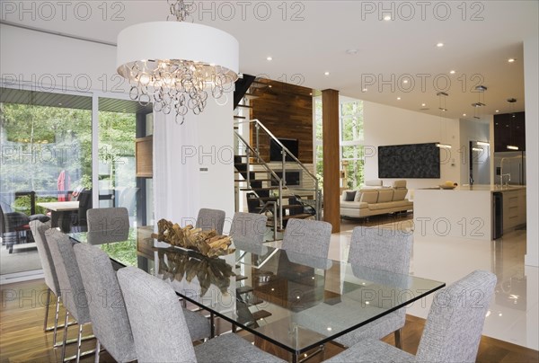 Glass dining table with gray upholstered high back chairs in dining room inside luxurious home,