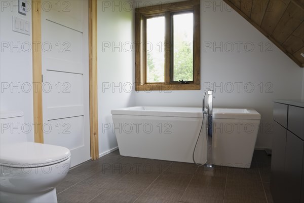 Main bathroom with grey ceramic tile floor and white porcelain toilet and freestanding bathtub on
