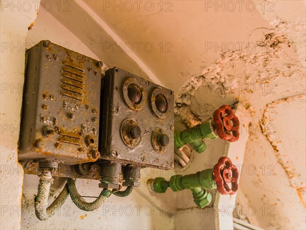 Closeup of rusted electrical circuit boxes and pressure valves with red handles attached to green