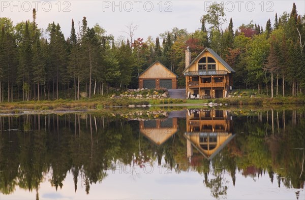 Garage and handcrafted two story spruce log cabin home with fieldstone chimney and green sheet