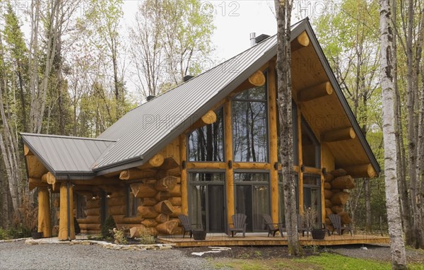 Luxurious Scandinavian style log home facade with large panoramic windows in spring, Quebec,