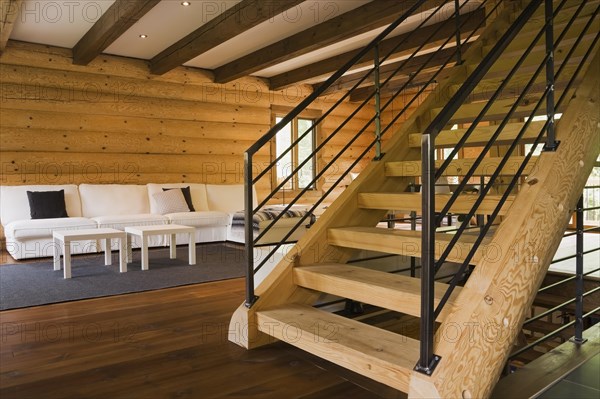 Wooden log stairs with black wrought iron railings and white cotton cloth upholstered sofas in