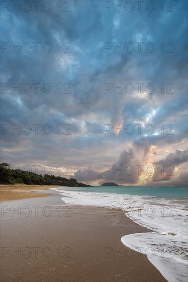 Lonely, wide sandy beach with turquoise-coloured sea. Tropical plants in a bay at sunset in the