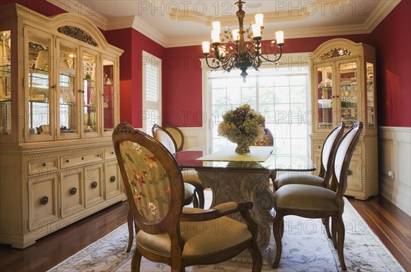 Glass top table with high-back wooden and upholstered chairs in dining room with buffets inside