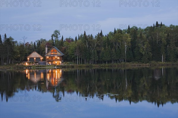 Illuminated two car garage and handcrafted two story spruce log cabin home with fieldstone chimney