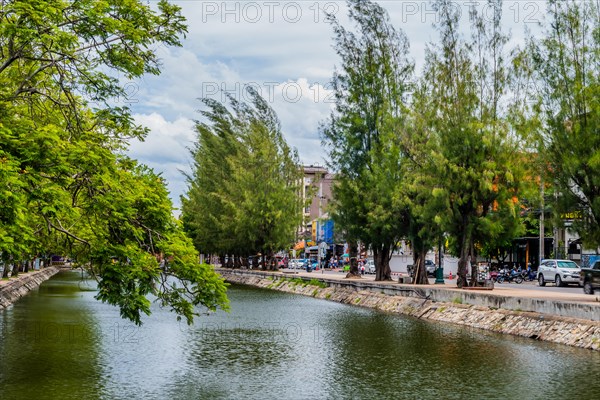 Cloudy sky reflecting on canal water, with a vibrant urban tree-lined waterfront, in Chiang Mai,