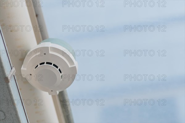 Electronic smoke detector on ceiling of enclosed pedestrian walkway with blurred plexiglass in