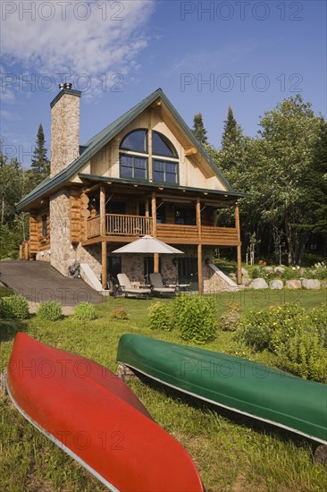 Handcrafted two story spruce log home cabin with fieldstone chimney, green sheet metal roof and red