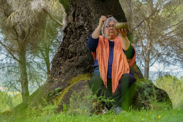 Mature woman with white hair meditating in the forest with her eyes closed and a Tibetan singing