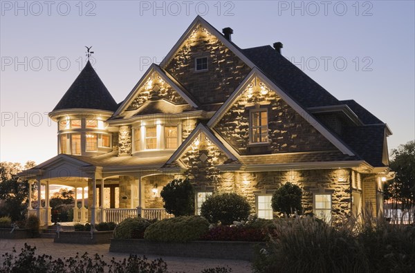 Elegant grey stone with white trim and blue asphalt shingles roof Victorian home facade at dusk in