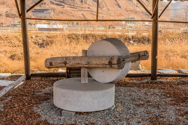 Old antique millstone and wheel in covered shelter with mountain community in background in South