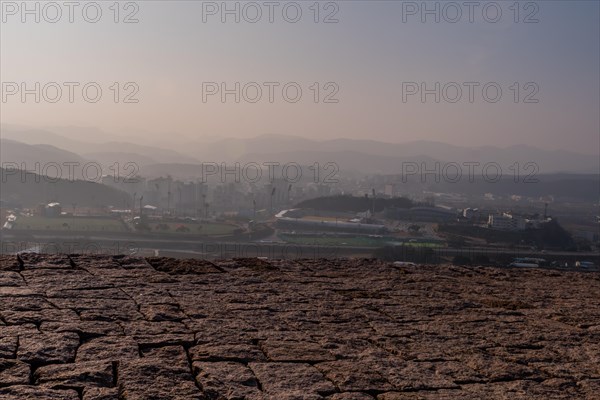 Top of mountain fortress wall made of flat stones with rural community under hazy sky in background