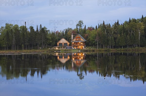 Illuminated two car garage and handcrafted two story spruce log cabin home with fieldstone chimney