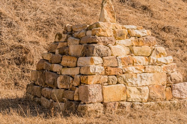 Closeup of pyramid shaped rock structure in field of brown grass at foot of hillside in Boeun,