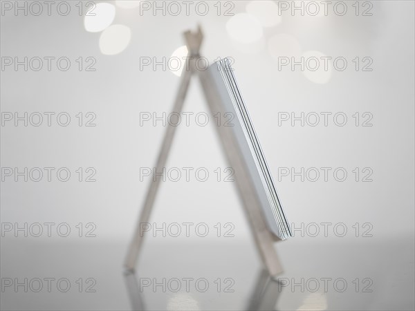 Mini easel in white made of wood, standing on a reflective smooth surface, white background with